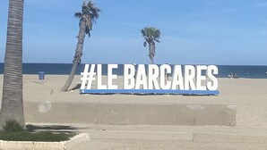 Ein Strand mit Palmen und einem Schild mit dem Text '#LE BARCARES'.