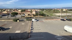 Ein Parkplatz mit mehreren Autos und einem weißen Lieferwagen, umgeben von Gebäuden und wolkenlosem Himmel.