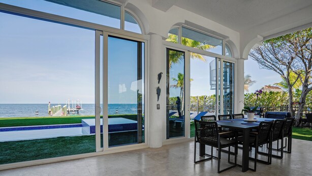 A spacious indoor area with a large glass door leading to a pool and a view of the ocean. - Exclusive Oceanfront Luxury Villa in the Keys (Key Largo)