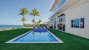 A swimming pool with artificial grass, palm trees, and a view of the ocean. - Exclusive Oceanfront Luxury Villa in the Keys (Key Largo)