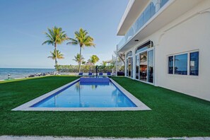 A swimming pool with artificial grass, palm trees, and a view of the ocean. - Exclusive Oceanfront Luxury Villa in the Keys (Key Largo)