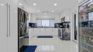 A modern kitchen with white cabinets, stainless steel appliances, a marble backsplash, and a view of the sea. - Exclusive Oceanfront Luxury Villa in the Keys (Key Largo)