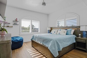 Un dormitorio con una cama, mesitas de noche, un tocador, una ventana con persianas y una planta en maceta.
