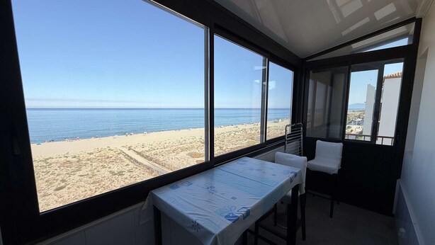 A room with a large window overlooking a beach, a small table with a tablecloth, and a chair. - Duplex with sea view, AC - 6 guests (Le Barcarès)
