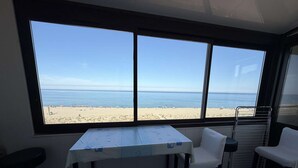 A room with a table and two chairs, a window with a beach view, and a radiator. - Duplex with sea view, AC - 6 guests (Le Barcarès)