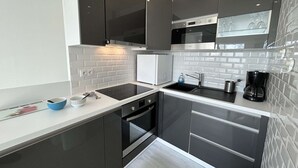 A modern kitchen with black cabinets, a white countertop, a built-in oven, and a coffee maker. - Modern apartment, dune view - 2 guests (Saint-Hilaire-de-Riez)