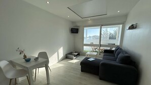 A modern living space with a dining area, a sofa, and a TV mounted on the wall. - Modern apartment, dune view - 2 guests (Saint-Hilaire-de-Riez)