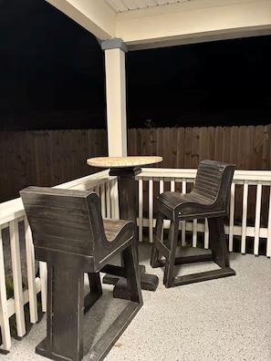 An outdoor patio with a round table and two chairs, a white railing, and a wooden fence in the background. - Lovely 2-bedroom house in St. Augustine perfect for your getaway (St. Augustine)