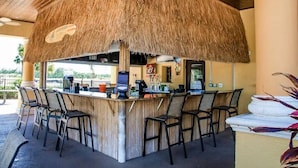Ett barområde med halmtak, barstolar och en bardisk, troligen en del av ett semesterresort eller hotell.