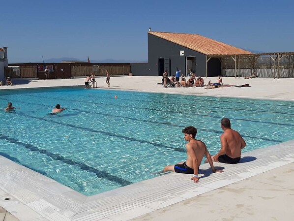 Una piscina con agua cristalina, un borde de baldosas y un edificio con techo de tejas rojas al fondo.
