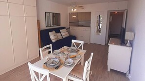 Un ambiente compatto con un tavolo da pranzo per due, un divano, angolo cottura e una televisione su un mobile.