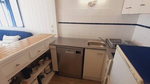 Una cucina compatta con lavello, lavastoviglie e microonde. Una finestra con persiane e un asciugamano blu sul piano di lavoro.