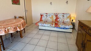 A room with a dining table, a sofa, a cabinet, and a door. - Apartment with port view - 4 guests (Gruissan)