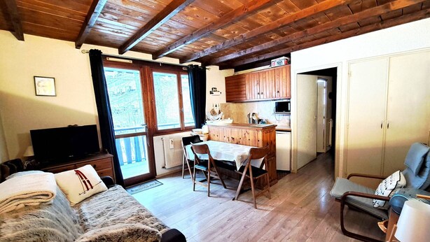 Ein gemütliches Zimmer mit Holzbalkendecke, einem Essbereich mit Tisch und Stühlen, einem Sofa mit Felldecke und einem Fernseher.