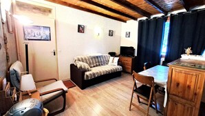 Ein gemütliches Zimmer mit einer Couch, einem kleinen Tisch, einem Stuhl, einem Schreibtisch und einem Fernseher.