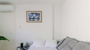 Une chambre à coucher avec un lit, une table de chevet avec une lampe, un climatiseur fixé au mur et un tableau encadré.