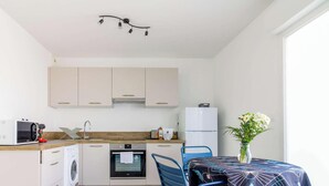 Une cuisine moderne avec des meubles blancs, un lave-linge, un four à micro-ondes et un réfrigérateur. On y trouve également un coin repas avec une table et des chaises, ainsi qu'un vase rempli de fleurs posé sur la table.