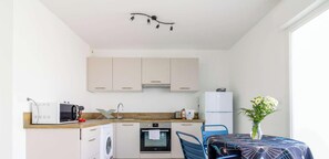 Eine kompakte Küche mit Mikrowelle, Backofen, Spüle und einem kleinen K ühlschrank. Ein Tisch mit Blumenvase und blauen Stühlen steht dort.