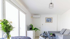 Un salon moderne comprenant un coin repas, un canapé gris, une petite table ornée d’un vase de fleurs et un luminaire suspendu.