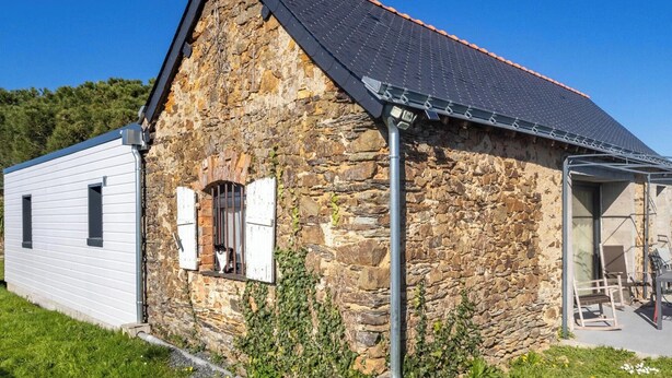 Ein Steinhaus mit geneigtem Dach, einem kleinen Fenster mit Fensterläden und einer Metallrinne.