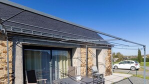 Ein Gebäude mit einer Fassade aus Stein, einer Glastür und einer Terrasse mit Gartenmöbeln.