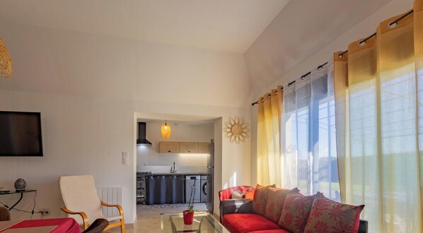 A living room with a sofa, a chair, a coffee table, and a TV. There is a kitchen in the background. - Cozy cottage near Angers - 5 guests (Chambellay)