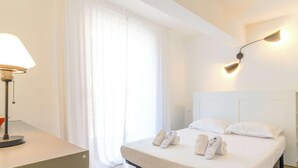 Hotellihuone, jossa on sänky, yöpöytä lampun kanssa ja seinään kiinnitetty valaisin.