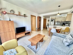 Ein modernes Wohnzimmer mit Fernseher, Sofa, Couchtisch und Essbereich.