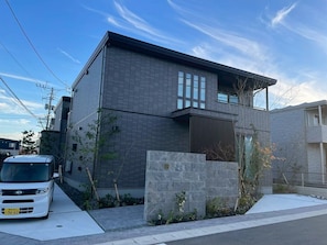 A modern two-story house with a stone facade, a car parked in front, and a clear sky.