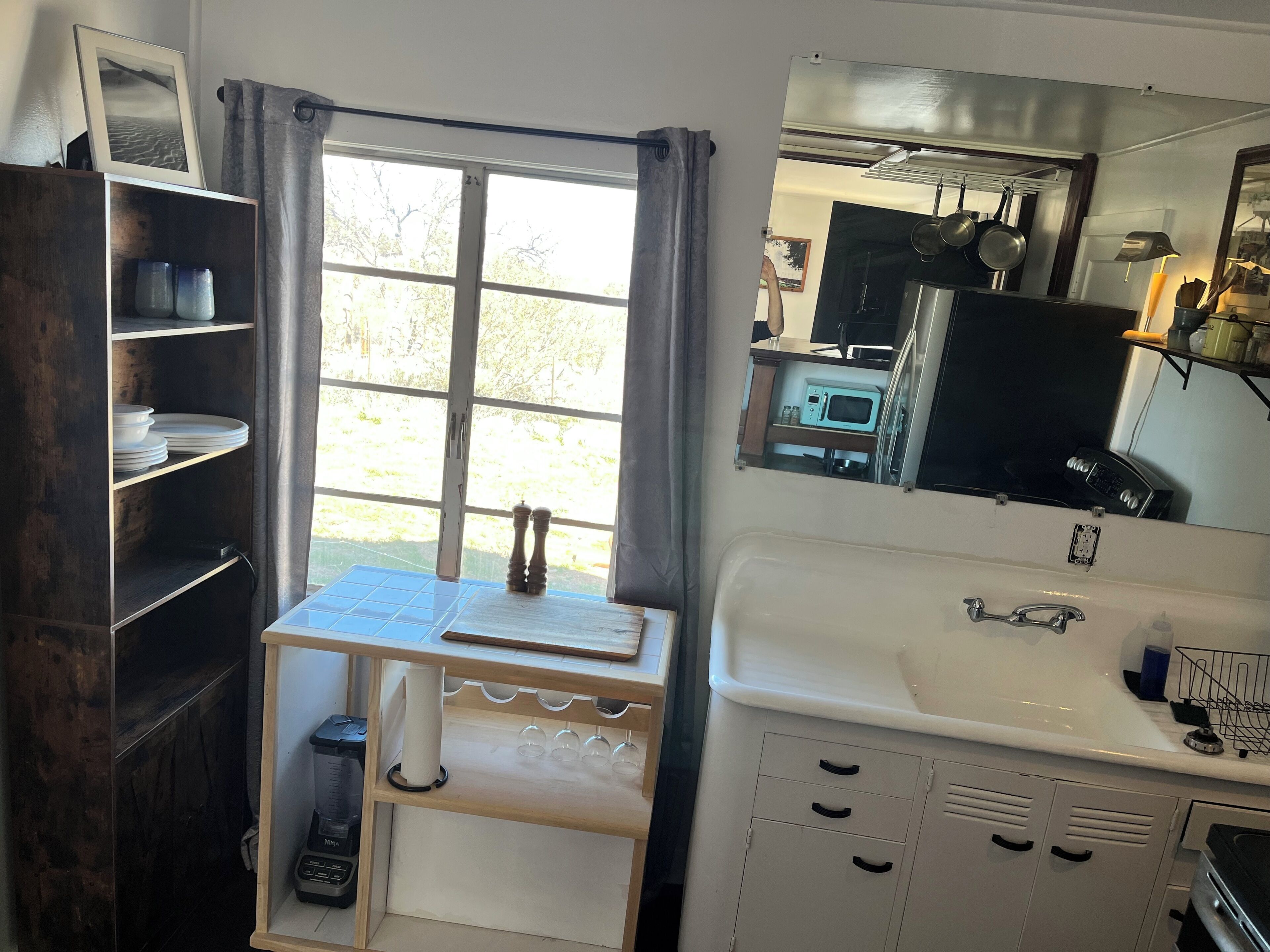 A compact kitchen with a window, a sink, cabinets, and a microwave.