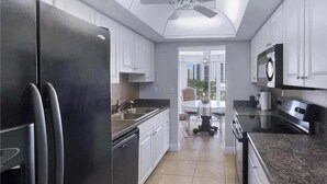 Une cuisine moderne avec un réfrigérateur noir, des armoires blanches, une table à manger et un ventilateur de plafond.