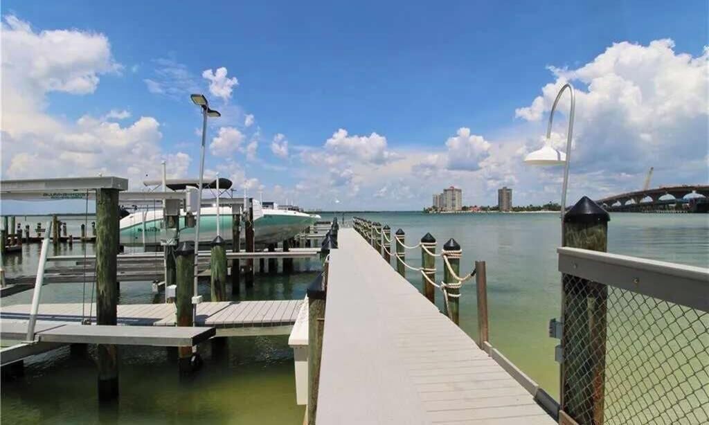 A waterfront dock with a clear view of the water, a bridge in the background, and a pedestrian walkway.