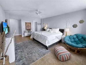 Ein Schlafzimmer mit Bett, Sessel, Teppich, Fernseher und Schreibtisch.