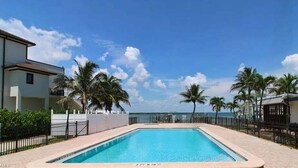 Une piscine avec vue sur l’océan, entourée de palmiers et d’une clôture.