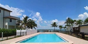 Ein Pool mit Blick auf das Meer, umgeben von Palmen und einem Zaun.
