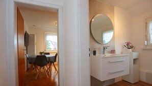 A modern kitchen with a round mirror, white cabinets, and a dining area with a table and chairs. - Apartment 35qm (Villingen-Schwenningen)