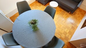 A round table with a grey tablecloth, surrounded by four grey chairs, in a room with wooden flooring and a grey sofa in the background. - Apartment 35qm (Villingen-Schwenningen)