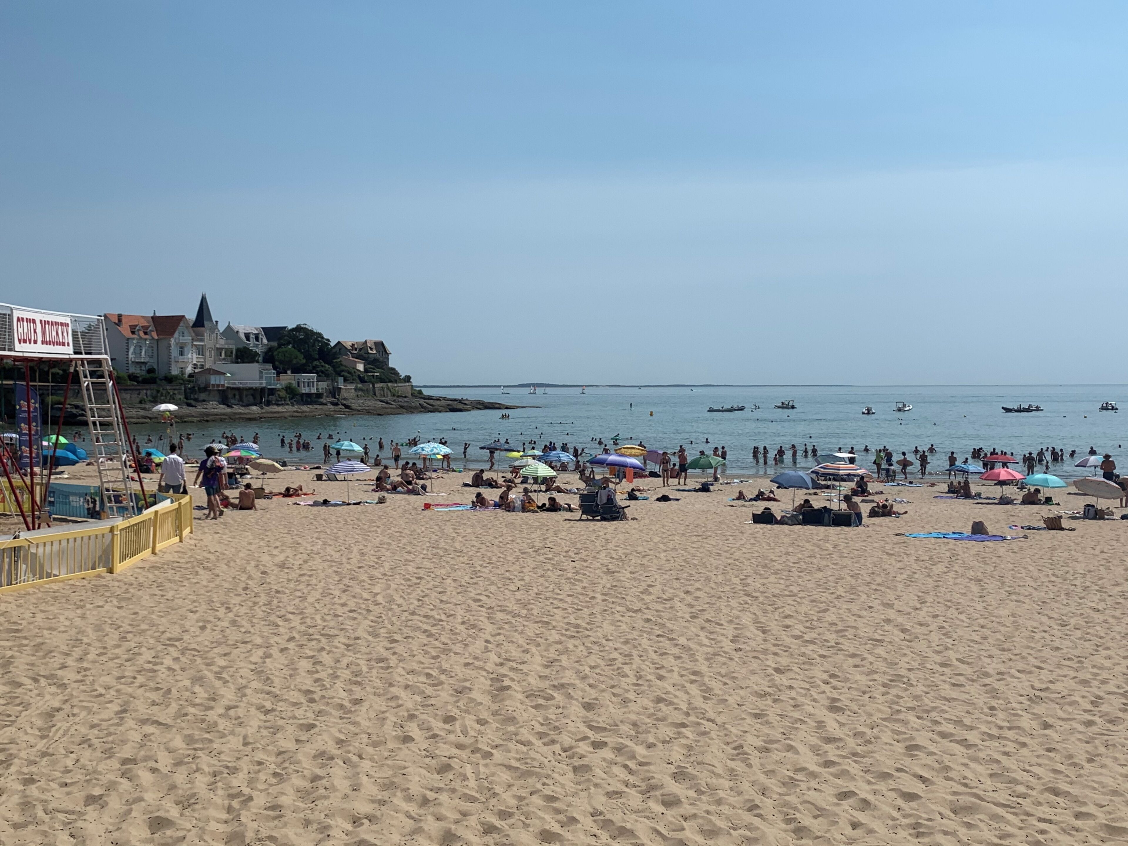 A beach with people, umbrellas, and boats.