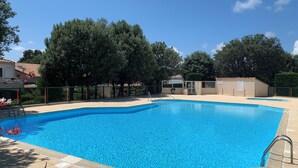 Ein rechteckiger Schwimmteich mit einer gefliesten Terrasse, umgeben von einem Zaun und Bäumen.