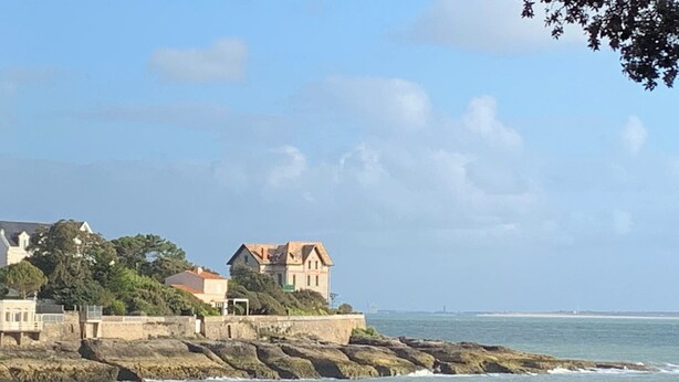 Eine Küstenlandschaft mit einer Steinmauer, einem Gebäude mit rotem Dach und dem Meer.