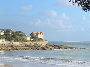 A coastal scene with a stone wall, a building with a red roof, and the ocean. - Villa beach and shops on foot (Saint-Palais-sur-Mer)