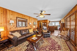 A wooden interior with a leather sofa, a rocking chair, a coffee table, and a patterned rug.
