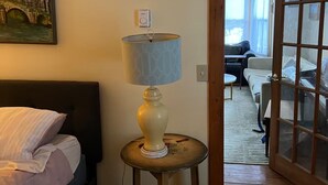 A bedroom with a bed, a lamp on a side table, a painting on the wall, and a view through an open door. - Near The Baseball Hall of Fame, Glimmerglass Opera and Dream Park Baseball Camp (Cherry Valley)