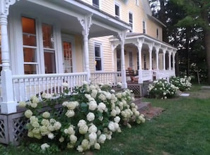 A two-story house with a porch and a garden with hydrangea bushes.