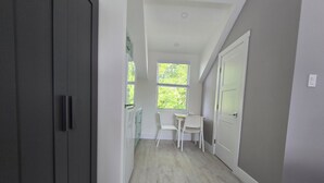 A hallway with a dark cabinet, a small table with chairs, and a window with a view of greenery. - Cozy Studio Centrally located in Grand Cayman near beaches,shops,and restaurants (Bodden Town)
