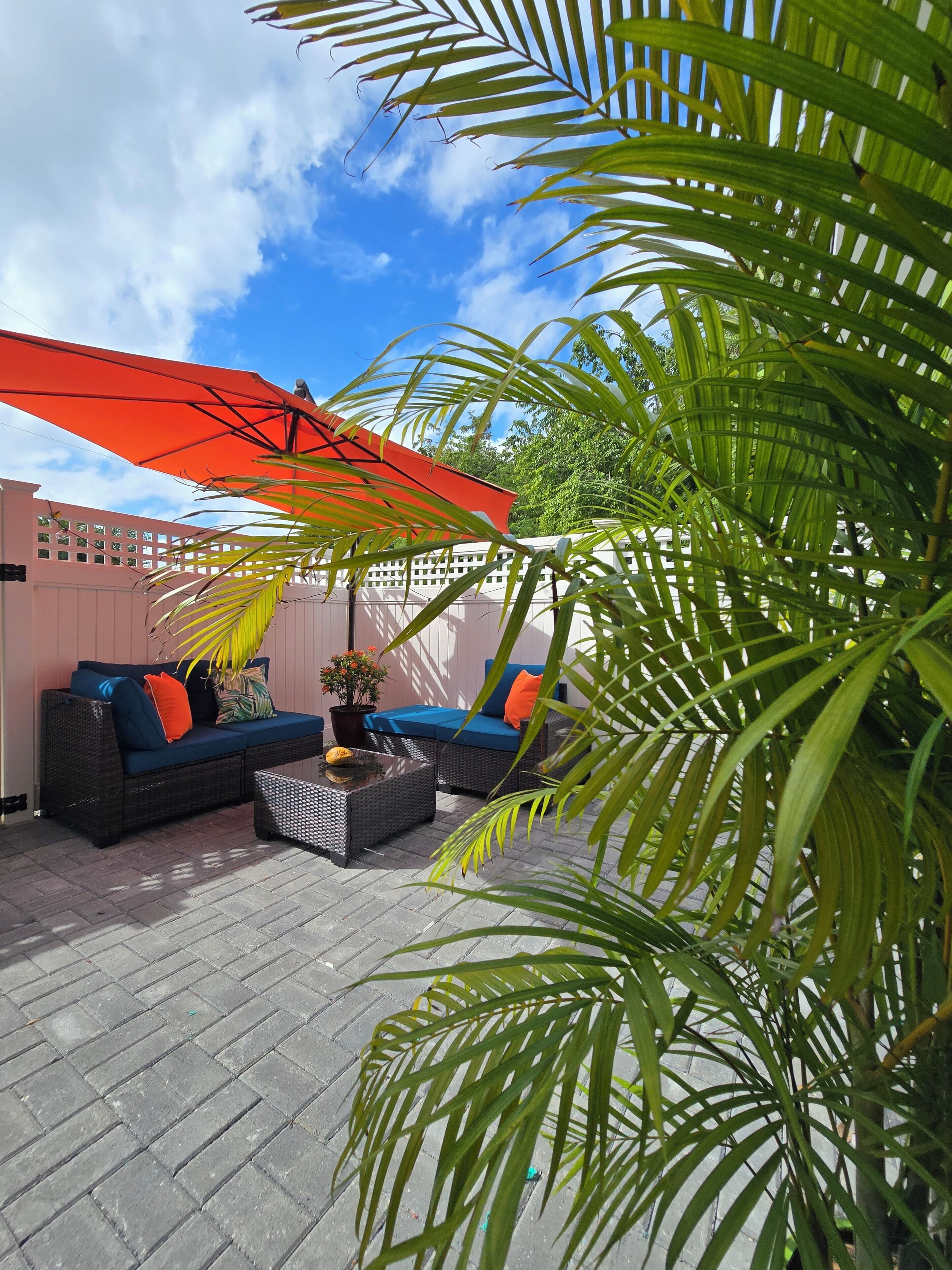 Eine Terrasse im Freien mit Korbmöbeln, einem roten Sonnenschirm und einem Blumentopf.