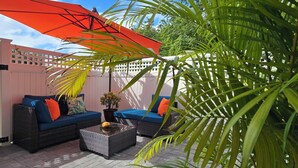 An outdoor patio with wicker furniture, a red umbrella, and a potted plant. - Cozy Studio Centrally located in Grand Cayman near beaches,shops,and restaurants (Bodden Town)