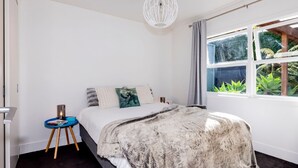 Ein Schlafzimmer mit einem Bett, einem Nachttisch, einem Fenster mit Vorhängen und einer Pendelleuchte.