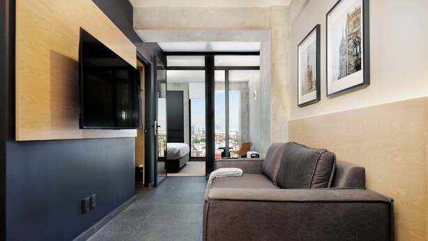 Un couloir d’hôtel moderne, avec un canapé, un téléviseur à écran plat et des tableaux encadrés accrochés aux murs.