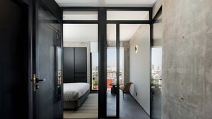 Un intérieur moderne avec un lit, une petite table et une chaise, ainsi qu’un balcon offrant une vue sur la ville.
